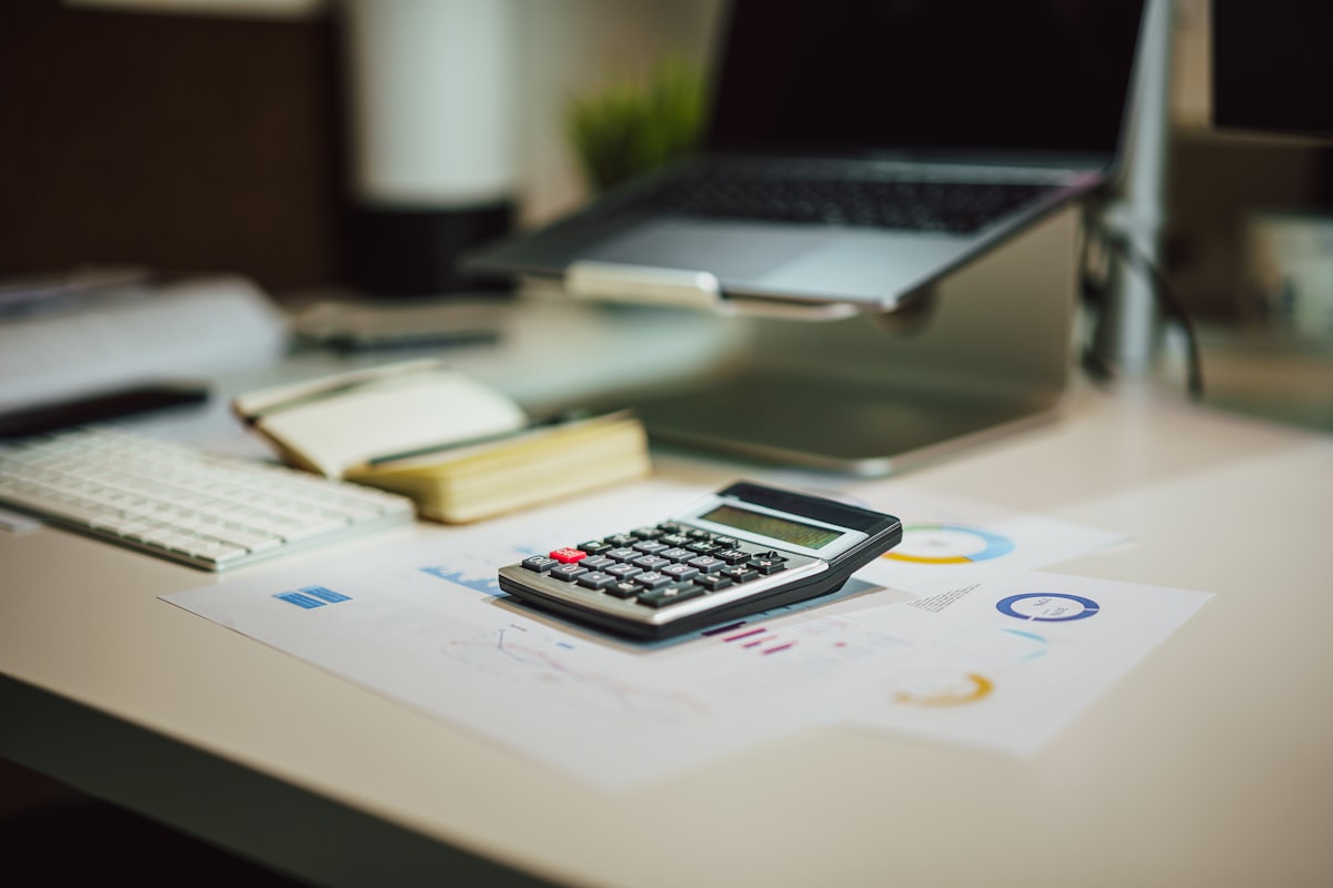 A calculator resting on a printed financial report beside a laptop on a tidy desk